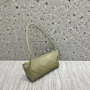 Light green woven leather crossbody bag with top zipper on a wooden surface