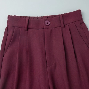 Detail of burgundy suit trousers with button closure and elegant pleated design