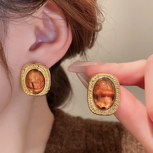 Close-up of vintage oval gold earrings with amber resin inlay and textured metallic edge