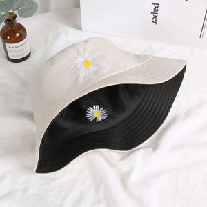 Close-up of daisy embroidery detail on a reversible cotton bucket hat in beige and black