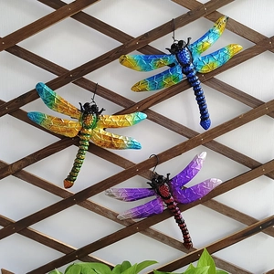 Set of three colorful metal dragonfly wall art hanging on a dark wood lattice backdrop