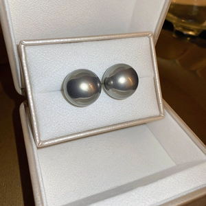 Détail de boucles d'oreilles perles rondes gris foncé dans un écrin beige doux