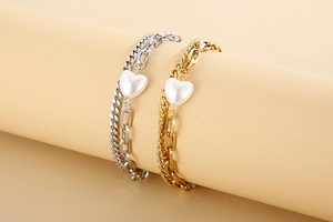 Detail of double-layer gold and silver bracelets featuring white heart-shaped charms