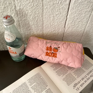 Detailed embroidery on pink quilted pencil case featuring a persimmon pattern and orange zipper