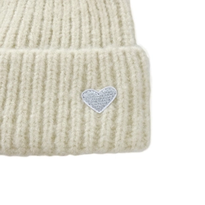 Close-up of off-white knitted texture with a silver heart embroidery on the beanie