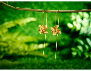 Macro detail of golden windmill drop earrings hanging on a branch with soft green foliage