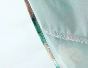 Vue macro des coutures fines et du tissu floral vert menthe sur l'ourlet de la robe