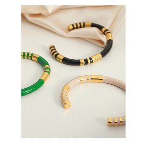 Detailed view of three enamel gold plated C-shaped bangles in green, black, and beige colors