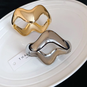 Macro shot of minimalist irregular wavy bangles in gold and silver mirror finish