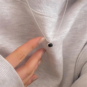 Close-up of minimalist silver chain with an oval black onyx pendant held by a model