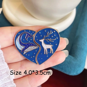 Close-up of heart-shaped enamel pin with starry whale and deer forest scenery