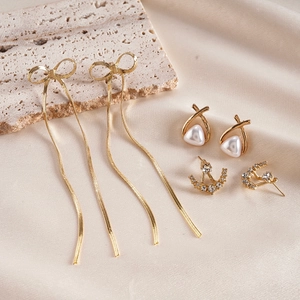 Detailed shot of three-pair gold earring set with bow tassels, pearls, and rhinestones