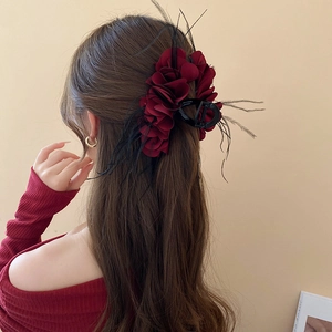 Detail view of a dark red layered flower hair claw with feathers on wavy hair