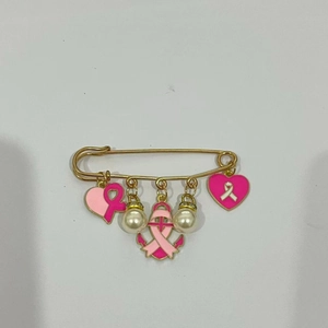 Détail de breloques cœur ruban rose et perles sur broche dorée contre le cancer du sein
