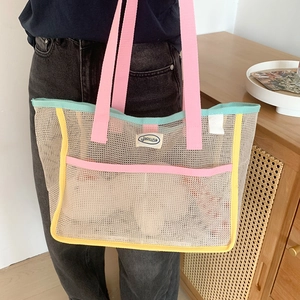 Mesh beach tote bag with pink straps and multi-color trim shown on a model indoors
