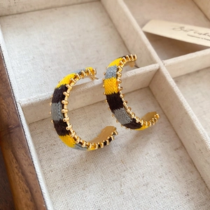 Macro shot of C-shaped knitted earrings with gold gear metal and colorful striped yarn