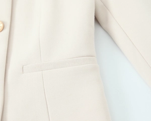 Dettaglio del blazer beige che mostra cuciture fini e un bottone dorato lucido rifinito