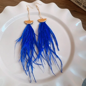Dettaglio di lunghi orecchini di piume blu con mezzelune dorate su un vassoio bianco