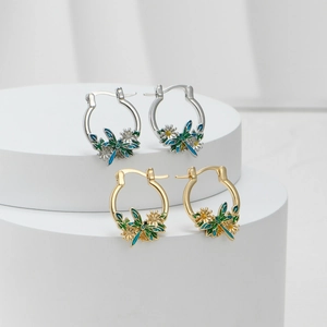 Macro detail of enamel dragonfly and floral earrings on white pedestal display