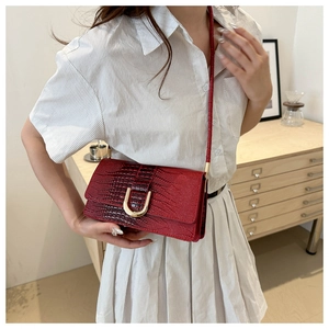 Détail d'un petit sac rouge à texture crocodile et boucles dorées sur un mannequin