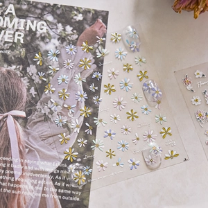 Detailed macro of 3D floral nail stickers with metallic daisy motifs on clear tips