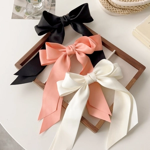 Three large satin bow hair clips in black, white, and pink on a vintage wooden tray