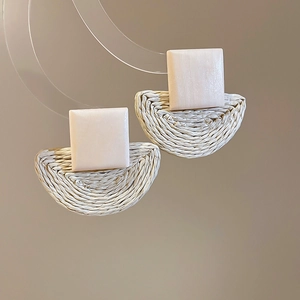 Detailed close-up of handmade raffia woven semi-circle drop earrings with pink square studs