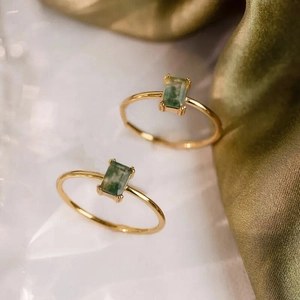Macro detail of two gold rings featuring rectangular green moss agate in claw settings
