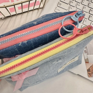 Detail of denim coin purses with colorful zippers and bow accents on a white keyboard