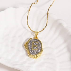 Macro shot of 18k gold plated letter E pendant with zircon stones on a white ceramic dish