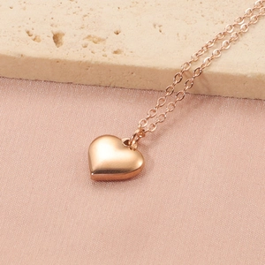 Gros plan d'un collier pendentif coeur en or rose avec chaîne croisée sur pierre
