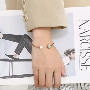 Adjustable gold flower bangle featuring a white shell pearl and green crystal charm
