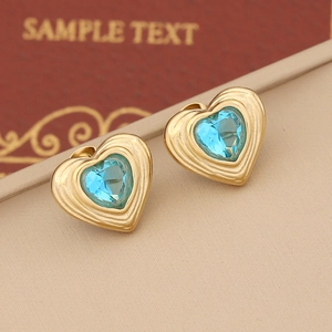 Golden heart stud earrings with concentric textures and central blue crystals on display