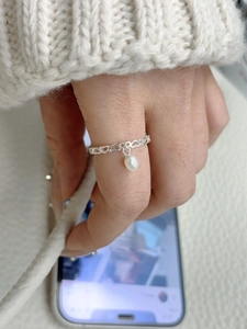 Detail of silver S925 heart chain ring with a pearl charm worn in a lifestyle setting