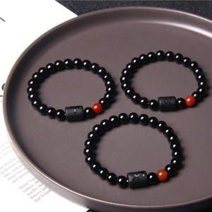 Detailed view of black stone bead zodiac bracelets with red agate in a ceramic tray