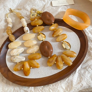 Macro view of vintage acrylic amber necklaces and orange resin bangle set on a wooden tray