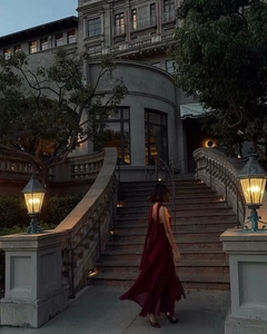 Elegant wine red halter neck dress flowing on stone steps by a classic European building