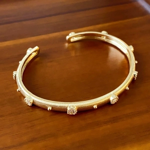Detail of golden open bangle with textured surface and inlaid small transparent crystals