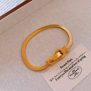 Détail du collier chaîne serpent dorée avec boucle magnétique sur fond en lin beige