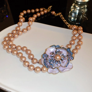Close-up of a double-layer pearl necklace featuring a floral pendant with blue and purple rhinestones