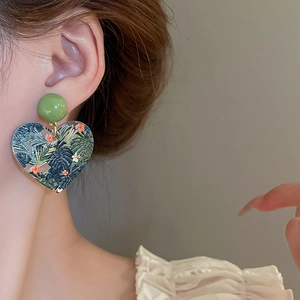 Close-up of heart earrings with green leaf and red flower print worn by a woman