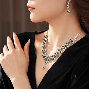 Close-up of elegant floral necklace and earring set with green gems and white diamonds