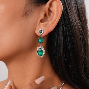 Close-up of vintage emerald green crystal drop earrings with sparkling diamond halo settings