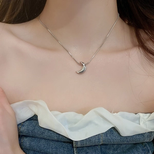 Close-up of a silver crescent moon pendant on a sleek snake chain worn on the collarbone