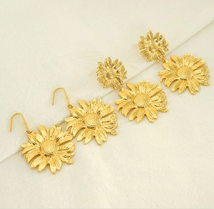 Macro detail of golden sunflower earrings featuring textured petals on white fabric