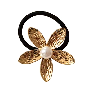 Minimalist gold flower hair tie with hammered petals and pearl accent on white backdrop
