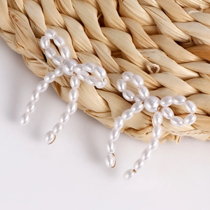 Close-up of handmade pearl bow earrings with intricate woven texture and golden metal links