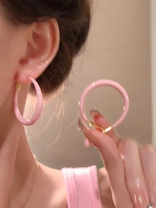 Close-up of pink enamel hoop earrings with gold clasp worn by a model for a summer look