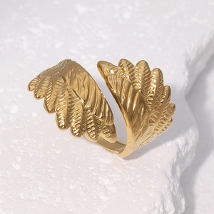 Golden stainless steel wing-shaped open ring with adjustable band on stone texture