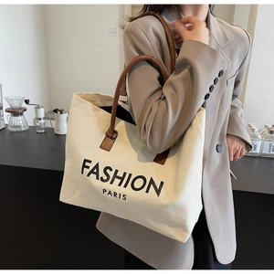 Canvas-Einkaufstasche mit FASHION-Logo und braunen Ledergriffen im Café-Ambiente